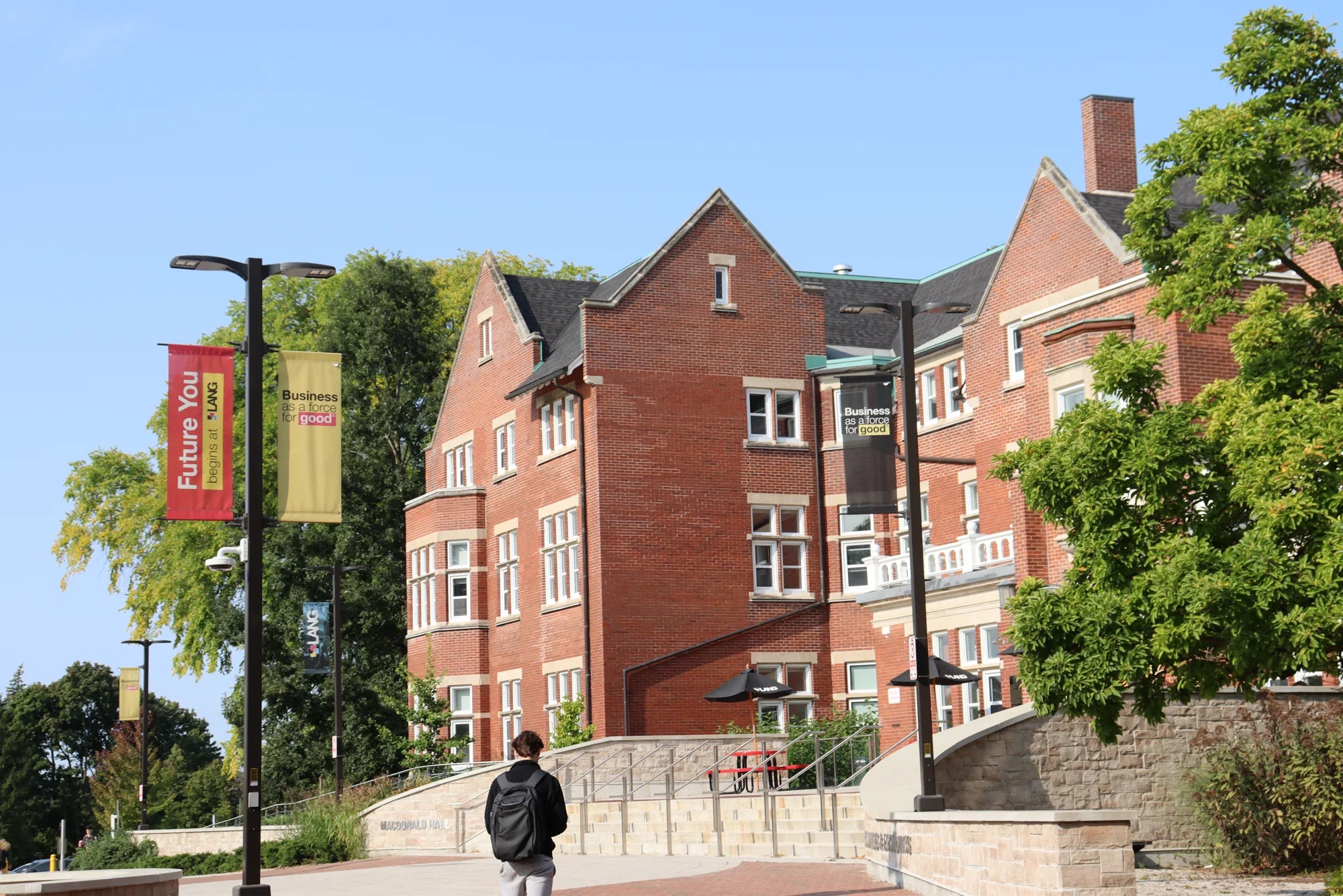 A student with a backpack walking toward Macdonald Hall, a red-brick Lang building, on a sunny day