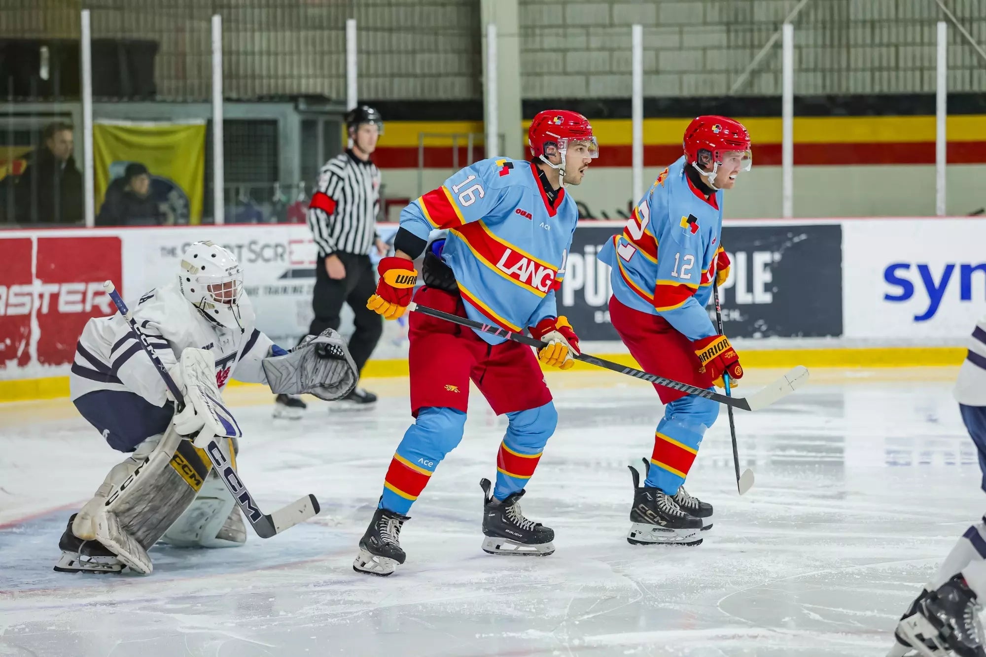 LANG hockey players in light blue and red on the ice, facing a goalie in white